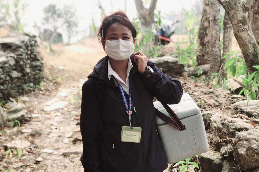 Kabita Chaudhari, senior health worker from Dhola Health Post in Jwalamukhi Rural Municipality, Dhading, on her way to the vaccination booth, carrying her ice-packed vaccine carrier. Credit : Chhatra Karki.