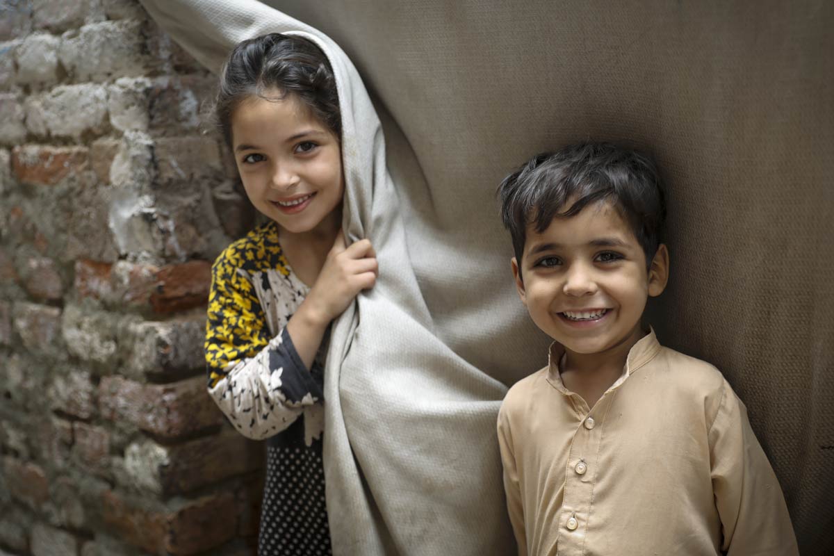 Parkha (10) with her brother Asif (5) stand outside their house observing health workers during the door-to-door polio campaign in Rasheed Garhi, Peshawar city, Khyber-Pakhtunkhwa province, Pakistan. Pakistan is a member of the OIC. Credit: Gavi/2023/Asad Zaidi